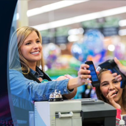 Smiling woman uses a phone to pay at a checkout while a girl watches nearby in a store.